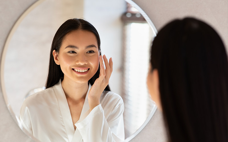 Asian woman cleaning face front of mirror