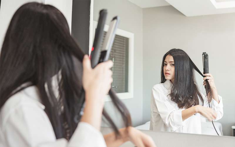 Image of a woman using hair straighteners in front of mirror