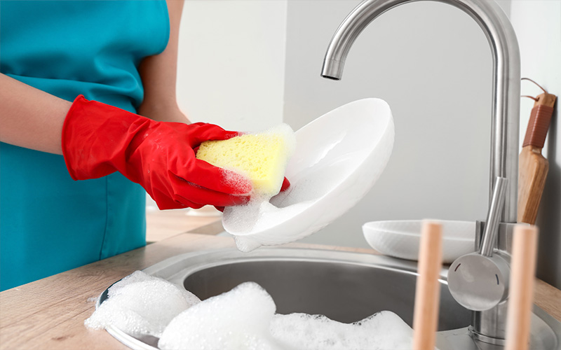 Close-up of a woman wearing protective gloves washing dishes with a sponge